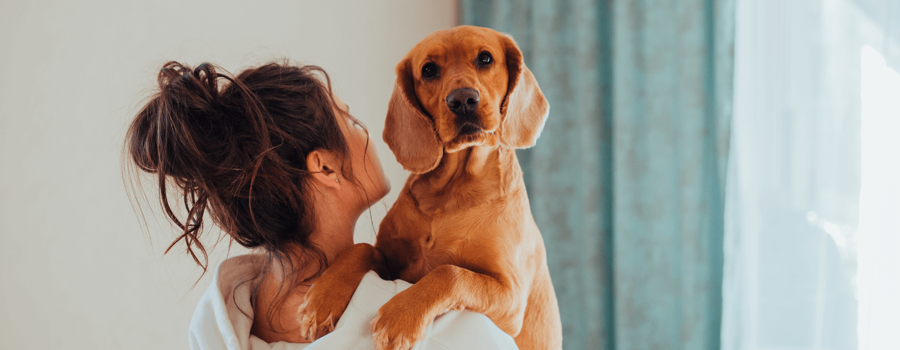 A woman with her hair in a bun holds a large golden-brown dog in her arms, both facing towards the camera.