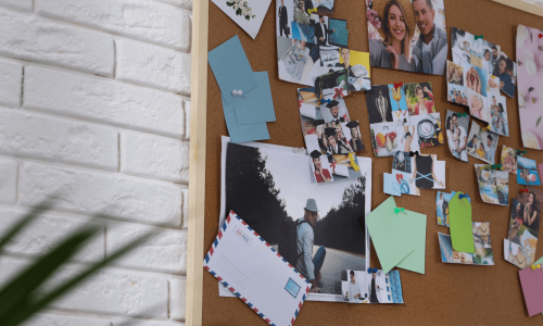 A corkboard decorated with photos, notes, and memories, creating a gratitude wall on a white brick background.