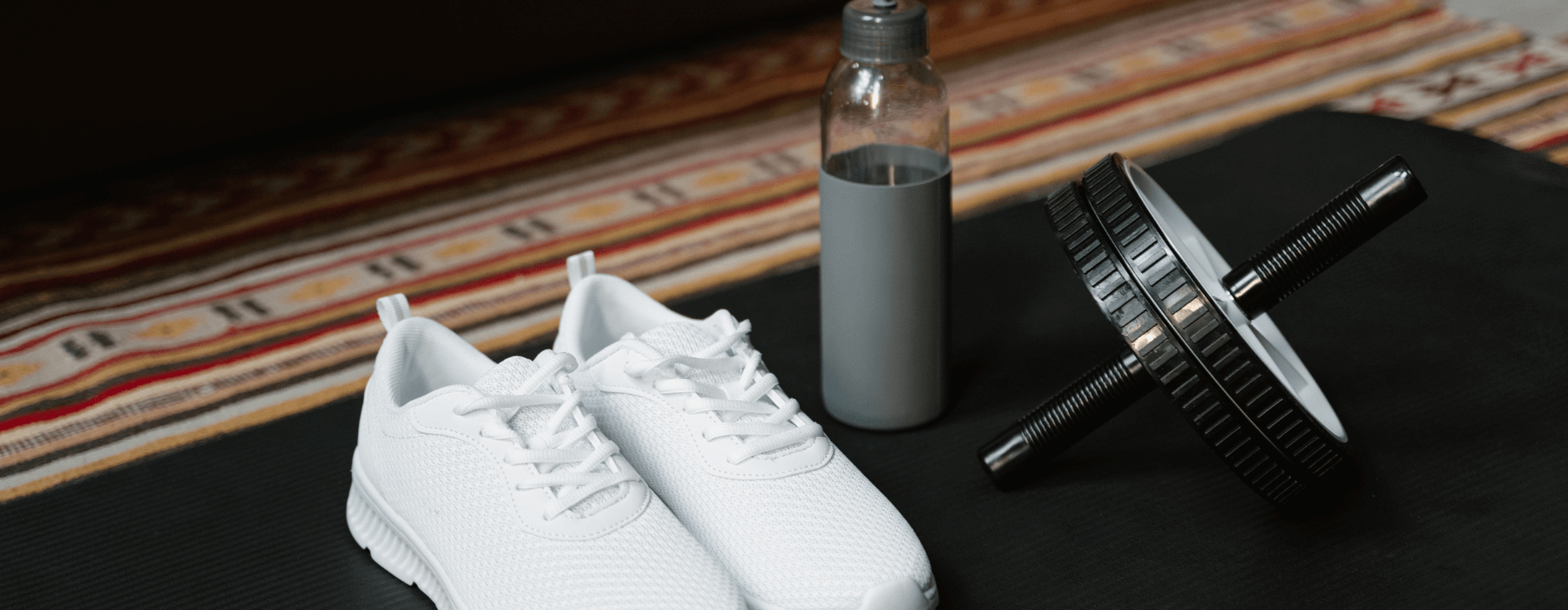 White athletic shoes, a water bottle, and an ab wheel are arranged on a workout mat.