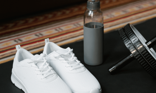 White athletic shoes, a water bottle, and an ab wheel are arranged on a workout mat.