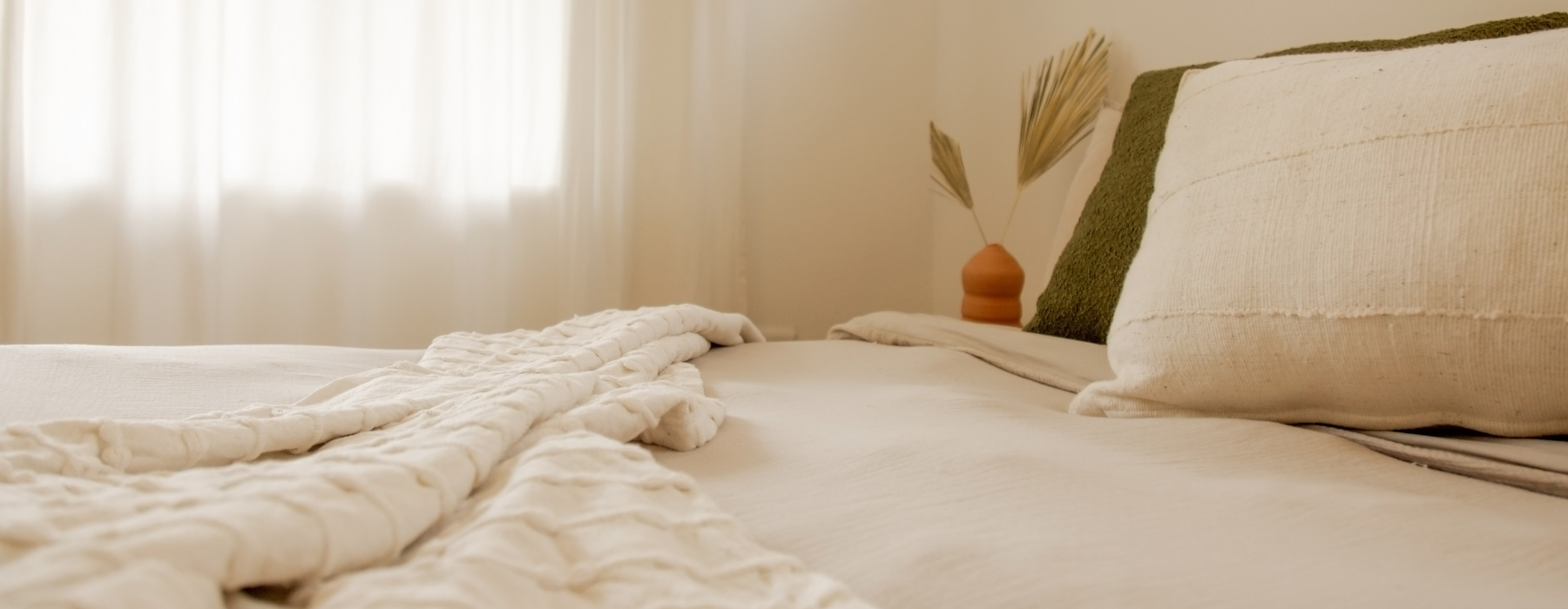 A cozy bedroom with neutral-toned bedding and soft natural light through sheer curtains.