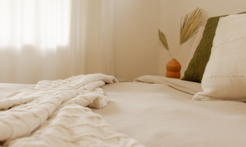 A cozy bedroom with neutral-toned bedding and soft natural light through sheer curtains.