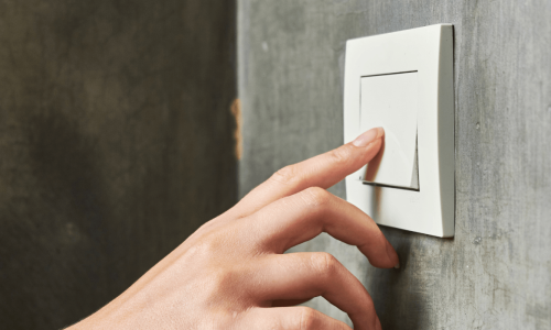 A hand is shown reaching towards and touching a light switch on a concrete wall.