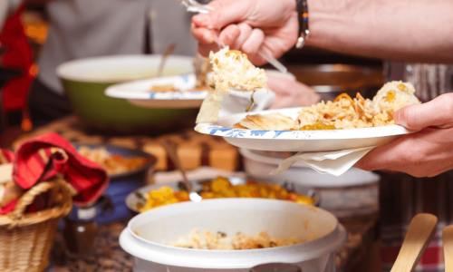 A person serving themselves from a variety of dishes at a potluck, representing a shared Friendsgiving meal.