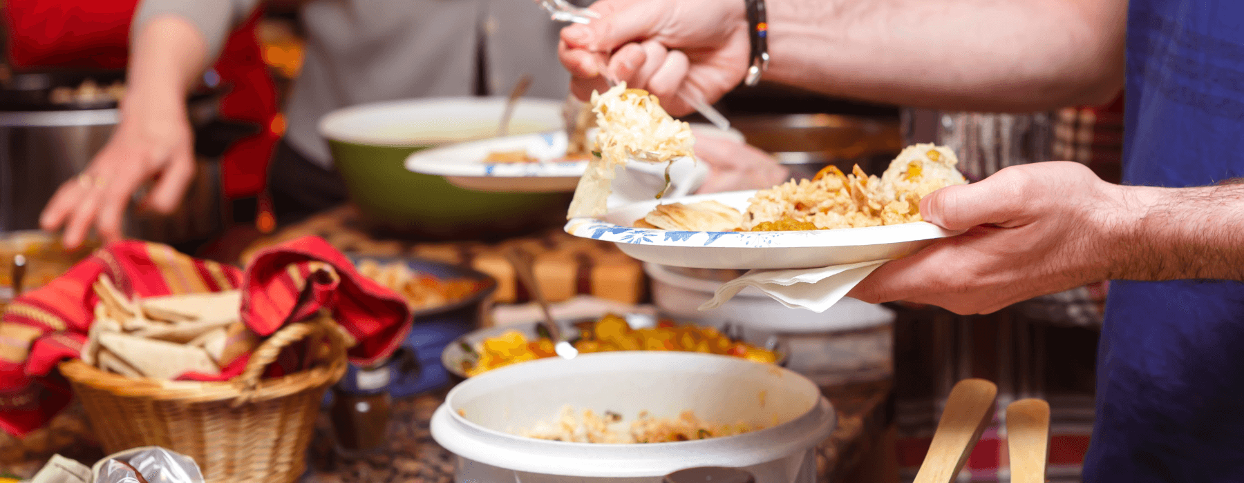 A person serving themselves from a variety of dishes at a potluck, representing a shared Friendsgiving meal.