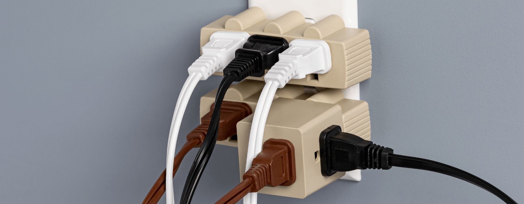 Multiple electrical plugs and cords overloading a single outlet in a wall.