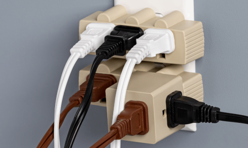 Multiple electrical plugs and cords overloading a single outlet in a wall.