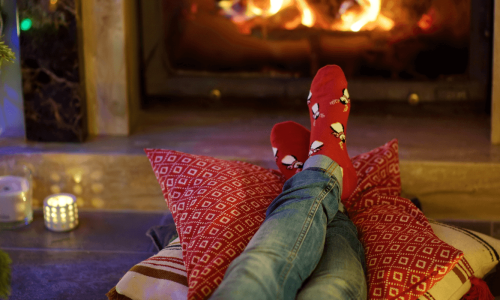 Cozy scene with someone relaxing by a fireplace, wearing festive socks.