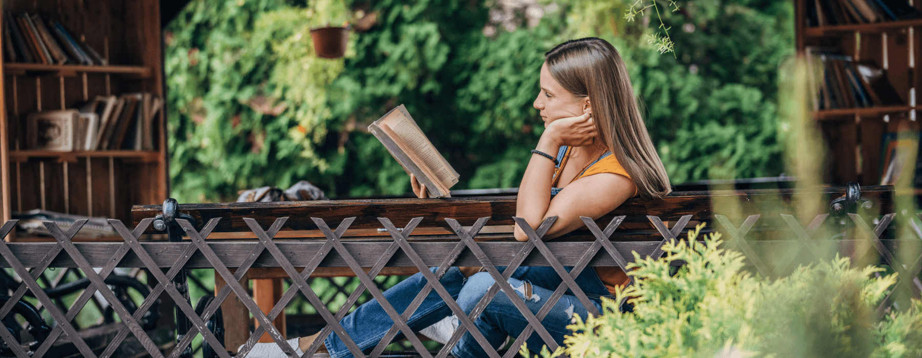 A woman sitting on an outdoor bench, surrounded by greenery and reading a book in a peaceful garden setting, enjoying a quiet moment.